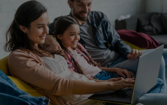 Imagem de um casal feliz sentados no sofá olhando para a tela de um notebook