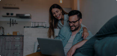 Imagem de um casal sorrindo, olhando para a tela de um notebook
