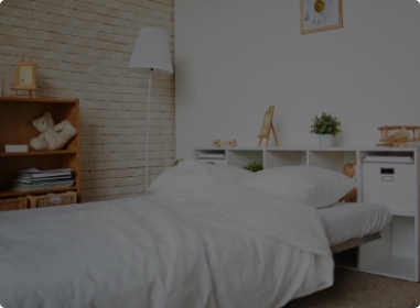 Imagem do quarto de uma casa, mostrando a cama e um estante ao fundo